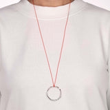 Runder Silber Anhänger mit rotem Band auf weissem Pullover