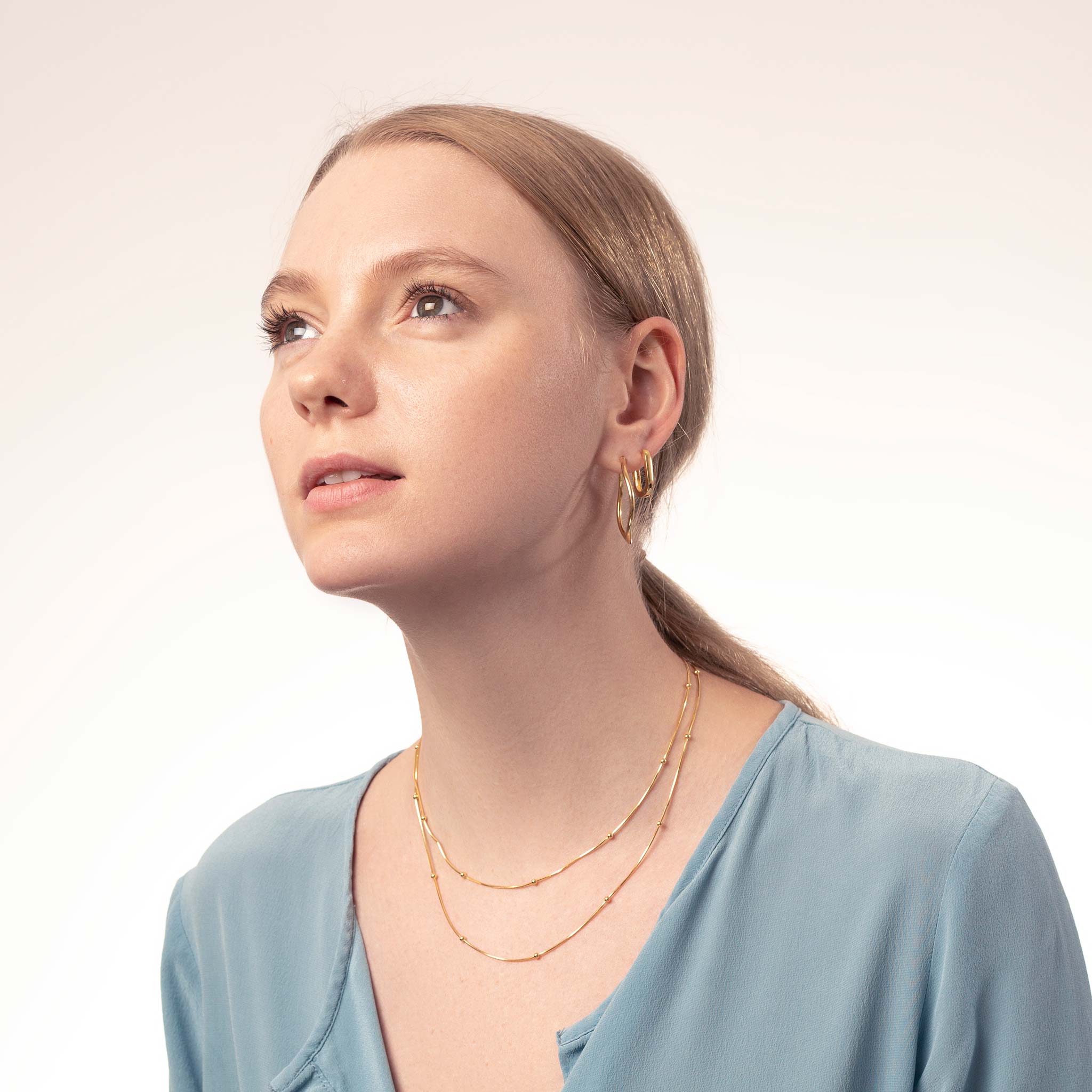 blonde Frau mit goldenen Creolen und zwei goldene Schlangenketten mit kleinen Kugeln